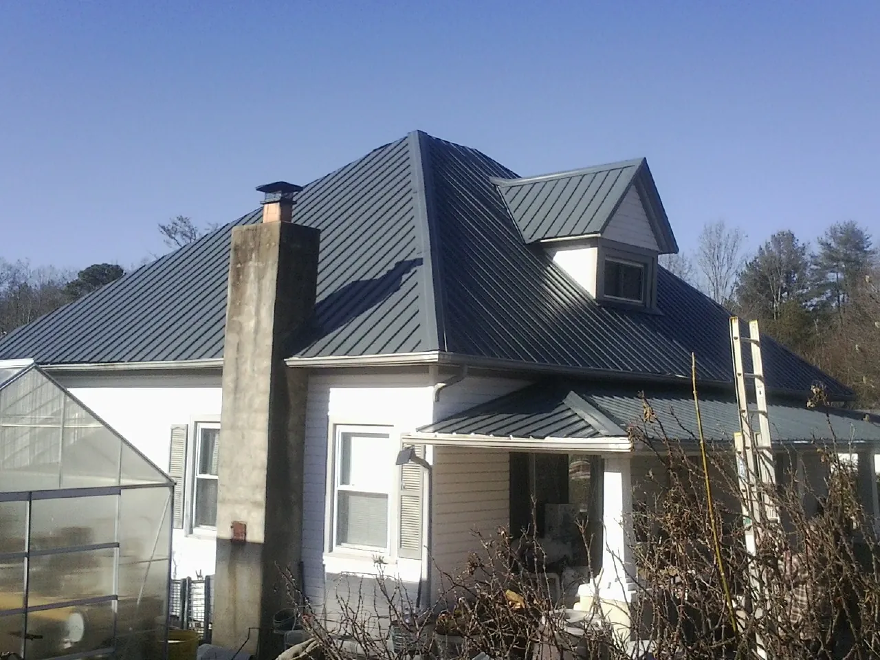Dark blue standing seam metal roof on a white farmhouse with dormer — Slate & Tile Roof Repair by Roofing Brothers in Prairie City