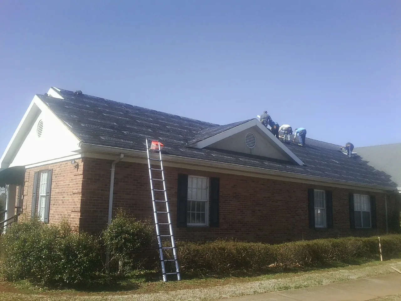 Crew tearing shingles off a brick ranch roof with a ladder set — Emergency Roof Repair work by our crew in Prairie City