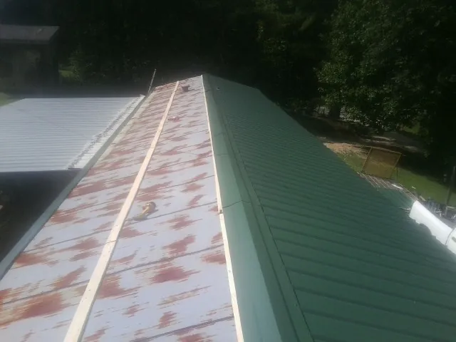 Old rusted panels beside newly installed green metal roofing — Wind Damage Roof Repair by Roofing Brothers in Prairie City