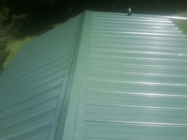 New green metal panels meeting at the ridge of a roof — Flat Roof Repair work by our crew in Prairie City