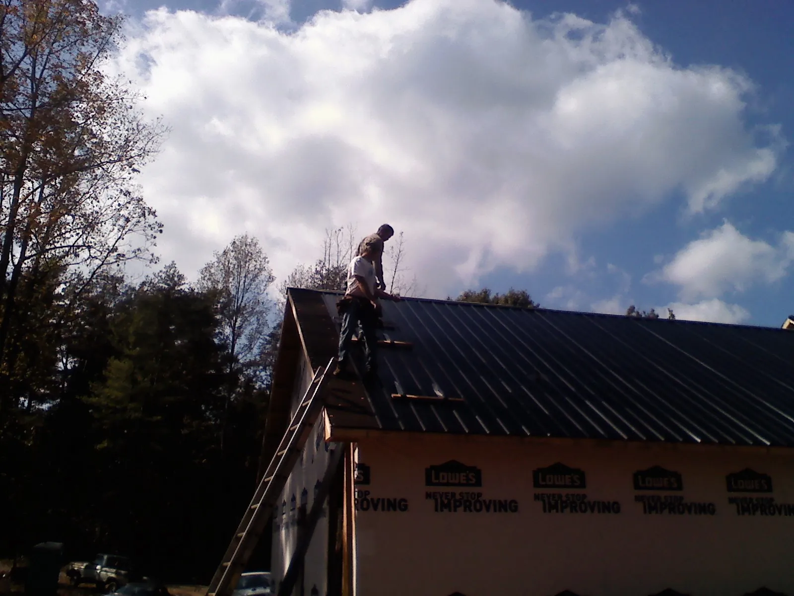 Roofer fastening dark metal panels high against a cloudy sky in Prairie City