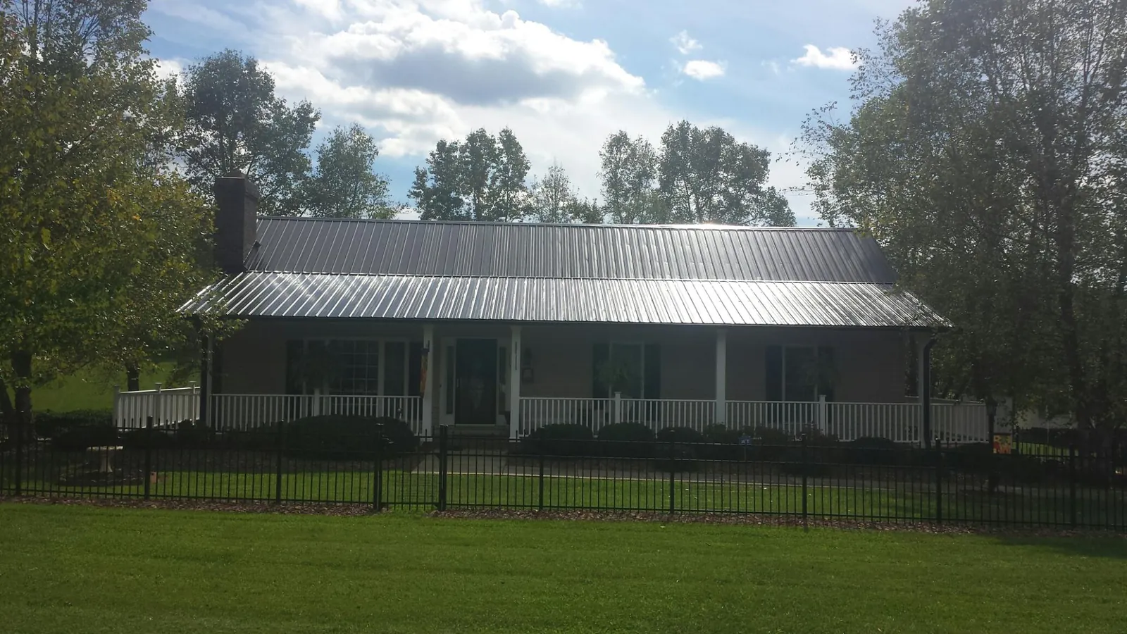 Gray metal roof on a brick ranch with a full width front porch — Gutter Guard Installation work by our crew in Prairie City